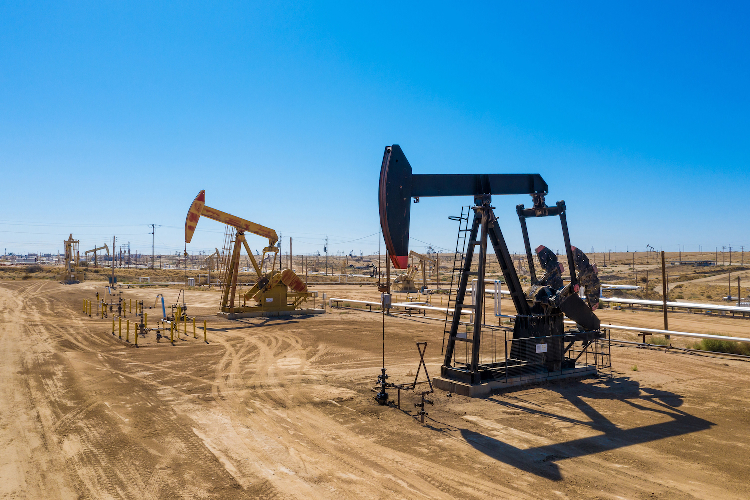 oil derrick pumps in a sandy field during the day with blue sky
